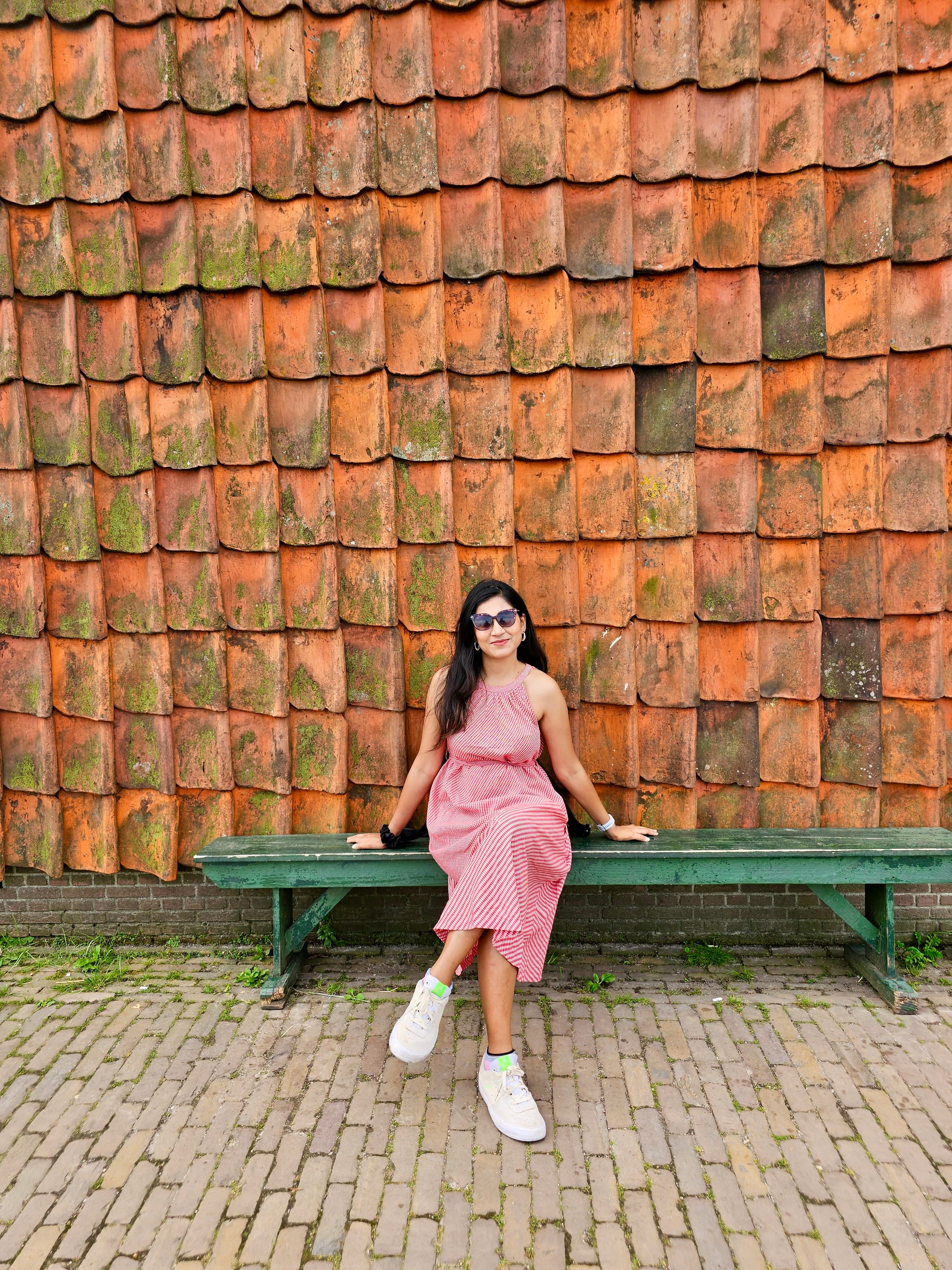A woman in a pink striped dress sitting against a rustic terracotta brick wall